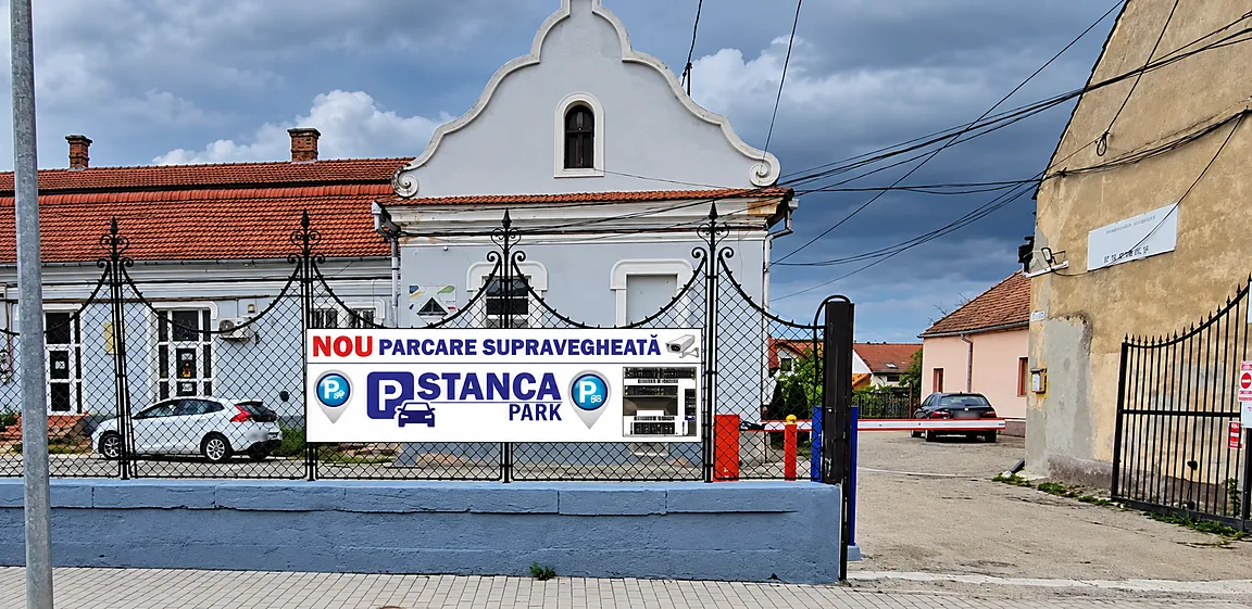Parcarea Stanca Park văzută din strada Doamna Stanca, Făgăraș, cu bannerul la gard și poarta de intrare